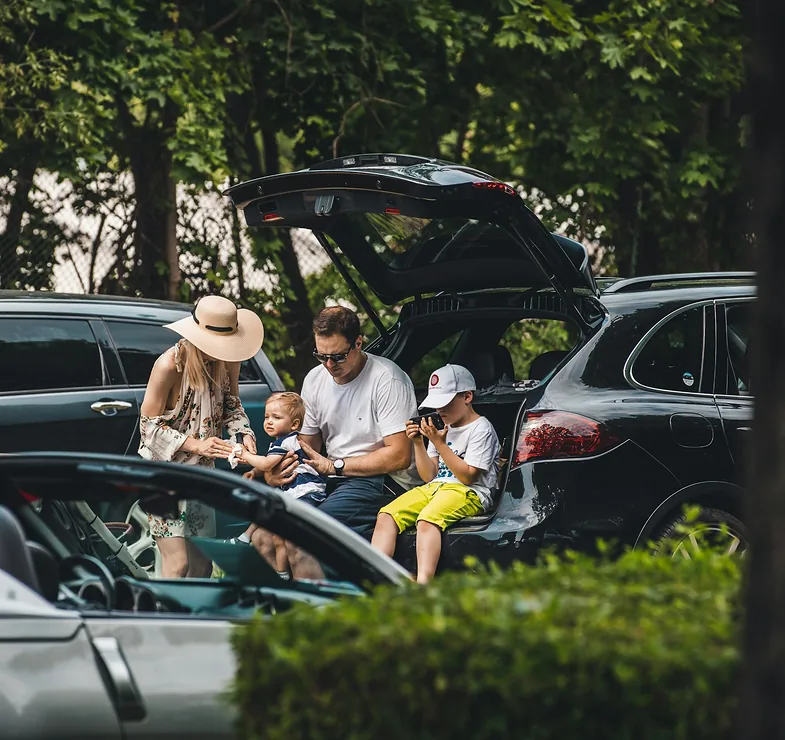 Šeima su vaikais užkandžiauja prie atidarytos automobilio bagažinės